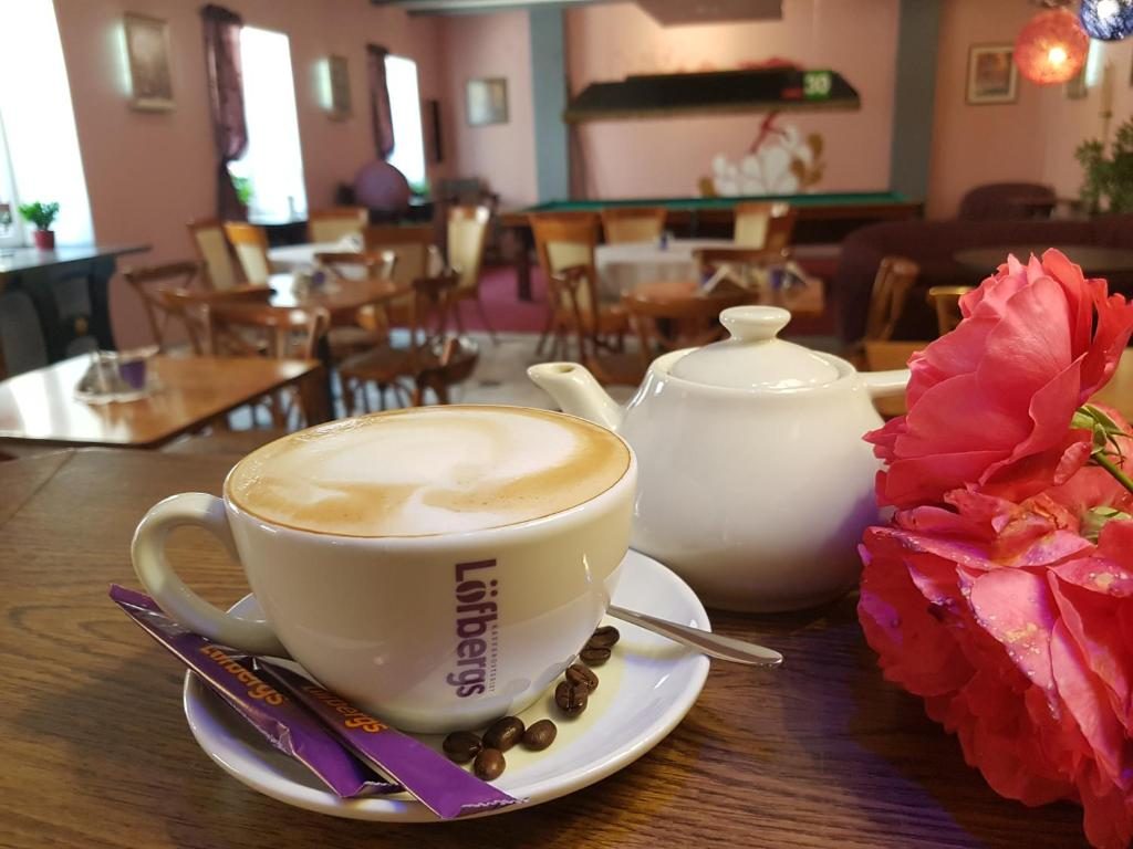 Cappuccino with coffee beans, a white teapot and pink roses on a table in the A1 Hotel Bar Lounge